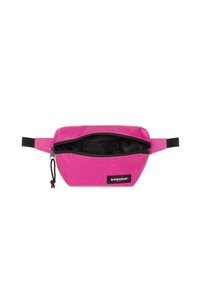 Ce sac banane en tissu rose vif présente une texture lisse. Il dispose d'un compartiment principal zippé et d'un petit patch logo à l'avant.