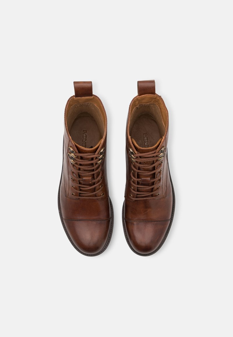 Stivali ankle in pelle marrone con una finitura liscia, dotati di punta rotonda, design con lacci, occhielli in metallo e un tassello sul retro.