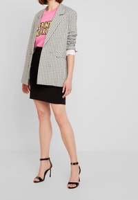 Rutig kavaj i vitt, svart och blått över en rosa grafik t-shirt, parat med en svart minikjol och svarta klacksandaler.