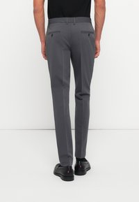 Gray trousers with a tailored fit, featuring two back pockets with button closures. Paired with black shoes, showcasing a smooth fabric texture.