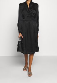 Musta mekko, jossa on chevron-tekstuuri, kietaisumalli ja pitkät hihat. Yhdistetty leopardikuvioisiin solkenauloihin ja pieneen mustaan käsilaukkuun.