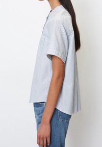 Ljust blårandig skjorta med korta ärmar, knäppkrage och lös passform, kombinerad med urblekta blå jeans. Diskreta sidslitsdetaljer.