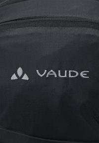 Zaino di tessuto nero con una superficie liscia e logo "Vaude" ricamato in argento con un accento triangolare. Dettagli della zip visibili.