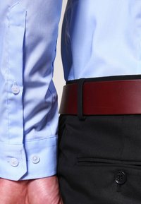 Ljusblå långärmad skjorta med knappmanchetter, kombinerad med svarta byxor och ett brunt läderbälte med en slät yta och rektangulär spänne.