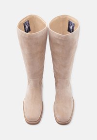 Paire de bottes hautes beiges en daim avec bouts carrés et coutures visibles, vue de dessus sur fond blanc.