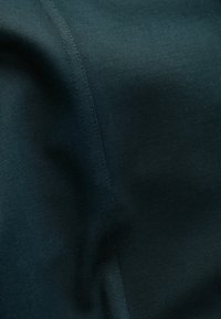 Tamsiai žalia medžiaga su lygiu paviršiumi ir subtiliu blizgesiu. Apvaduose yra smulkūs siūlai, suteikiantys elegantišką, vienodą išvaizdą.