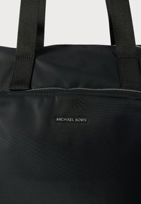 Borsa tote nera in nylon con due manici in tessuto, caratterizzata da un logo argento e dettagli con zip nella parte anteriore. Texture liscia, design minimalista.