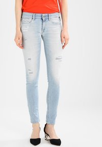 Light blue skinny jeans with distressed details and fading. Features classic five-pocket styling and a zip fly. Worn with black heels.