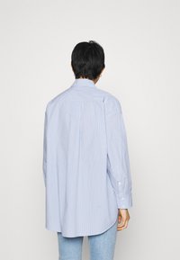 Blue and white striped shirt with a high collar, long sleeves, and rounded hem. Made of lightweight fabric, featuring buttoned cuffs.