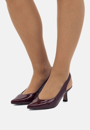 Tacones slingback de charol burdeos con punteras afiladas, tacones bajos tipo bloque y un corte transparente a los lados. Textura suave.