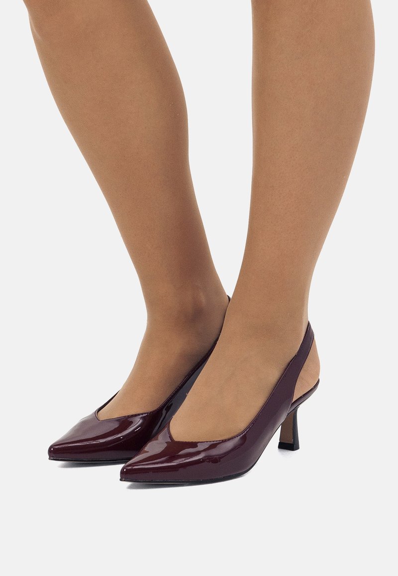 Tacones slingback de charol burdeos con punteras afiladas, tacones bajos tipo bloque y un corte transparente a los lados. Textura suave.