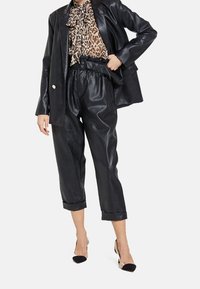 Blazer en cuir noir associé à un chemisier imprimé léopard et un pantalon en cuir noir taille haute, avec une taille ceinturée et des ourlets retroussés.