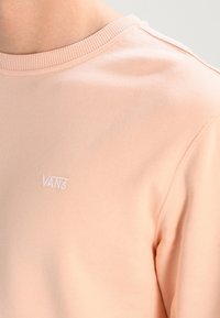 Sudadera de cuello redondo en melocotón claro con pequeño logotipo de Vans bordado en blanco en la parte superior izquierda del pecho.