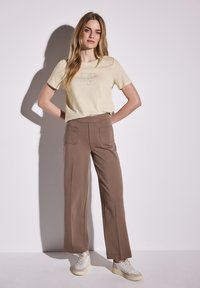 Khaki tričko s krátkým rukávem s texturovaným potiskem a hnědými širokými kalhotami, doplněné teniskami. Jednoduchý design, hladká látka, volný střih.