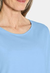 Helles blaues T-Shirt mit kurzen Ärmeln, glatte Textur, Rundhalsausschnitt und lässiges Design. Fokus auf dem Nacken- und Schulterbereich.