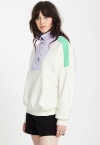 Weißer Pullover-Sweatshirt mit lila-grünem Farbblockdesign, ausgestattet mit einem hohen Kragen, Kordeln und gerippten Bündchen.