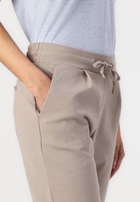 Beige joggerbyxor med elastisk midja, dragsko, sidfickor och en texturerad tyg, visade vilande mot en ljusblå skjorta.