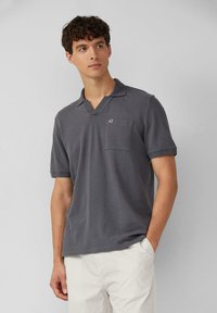 Szara polo z krótkim rękawem, z dekoltem w serek, z teksturowanej tkaniny i kieszonką na piersi. Posiada małe logo po lewej stronie, blisko kołnierza.