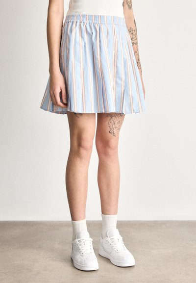 Jupe rayée bleue avec des rayures verticales roses et blanches, design plissé, taille élastique ; associée à des baskets et des chaussettes blanches.