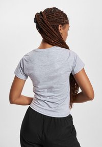 T-shirt grigia aderente realizzata in tessuto misto cotone, con maniche corte, scollo rotondo e texture liscia. Indossata con pantaloni neri larghi.
