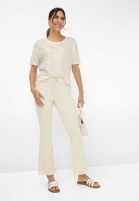 Lichtbeige gestreepte top met korte mouwen en metallic draden, gecombineerd met crèmekleurige wijde broek en witte slipper-sandalen; met een kleine handtas.