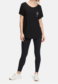 Svart kortärmad t-shirt med rundad halsringning och vit text "Idag är jag glad" på bröstet, tillsammans med svarta leggings och sneakers.