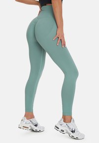 Hoogwaardige mintgroene leggings gemaakt van rekbare stof met een gestructureerd naaddetail en een witte logo-accent. Gecombineerd met witte sport schoenen.