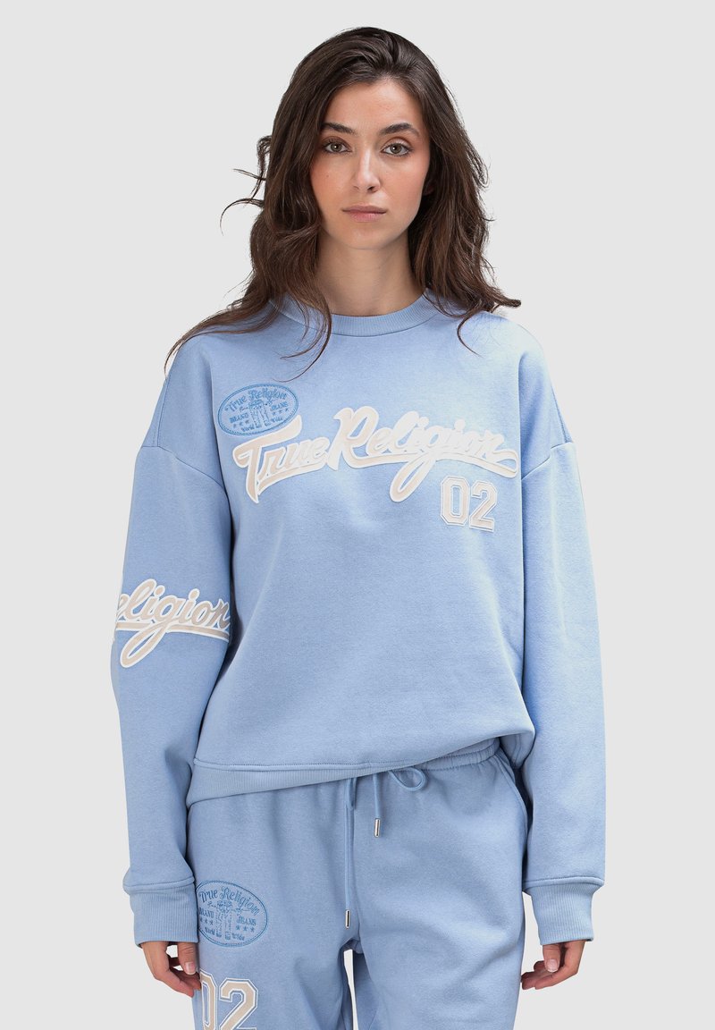 Sweat-shirt bleu clair avec logo "True Religion" brodé en blanc et numéro "02". Présente des poignets côtelés et une coupe décontractée.