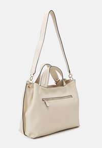 Beżowa skórzana torebka z fakturowaną powierzchnią, przednią kieszenią na suwak oraz długim paskiem z czarnymi krawędziami. Dwa małe uchwyty u góry.