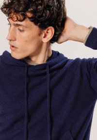 Hoodie bleu marine en tissu doux, avec une coupe décontractée, des cordons de serrage au cou et une finition texturée. Design simple avec des accents subtils.