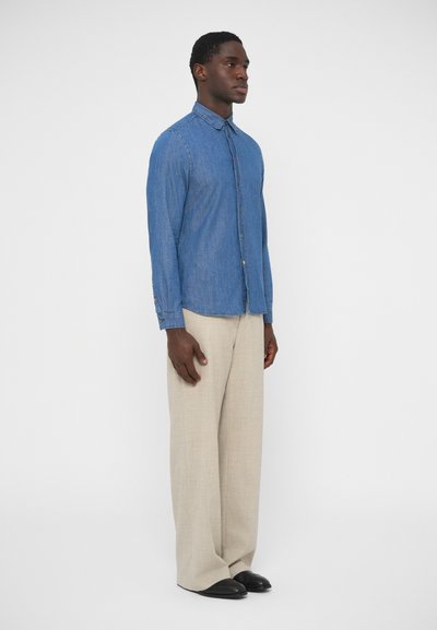 Világoskék farmering hosszú ujjakkal, gombos elülső résszel és hegyes gallérral. Bézs színű, bőszárú nadrággal és fekete cipőkkel párosítva.