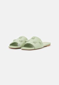 Sandali leggeri verde chiaro con punta aperta, caratterizzati da un design trapuntato e piccoli dettagli quadrati sulla parte superiore, suola piatta con una base color beige.