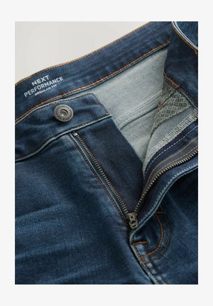 Tamsiai mėlyni džinsai su reguliariais pritaikymu, turintys užtrauktuką, metalinį mygtuką ir kontrastingas oranžines siūles. Viduje yra šviesiai mėlynas pamušalas.