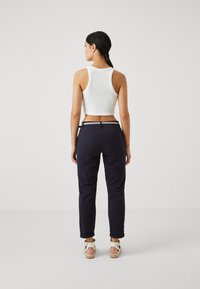 Bijeli rebrasti crop top, tamnoplave hlače s preklopima, srebrni detalji na struku i svijetle sandale s trakama.