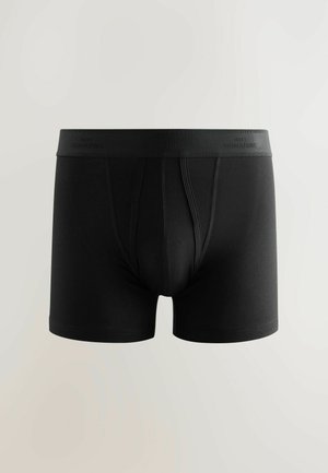 Boxer cortos de algodón negros con una suave cinturilla elástica que lleva el texto "NEXT SIGNATURE". Textura suave y diseño ajustado.