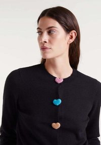 Schwarze Strickjacke mit rundem Ausschnitt, ausgestattet mit vier herzförmigen Knöpfen in Pink, Blau, Braun und Creme. Weicher Stoff, schlichtes Design.