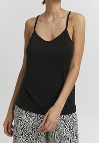 Czarna koszulka na ramiączkach z cienkimi paskami i dekoltem w kształcie litery V, wykonana z miękkiego materiału. Połączona z spodniami w czarno-białym wzorze zebry.