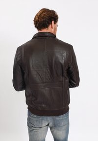 Hnědá kožená bunda s hladkou texturou, stojatým límcem a žebrovaným lemem. Má švové detaily na zádech a ramenech.
