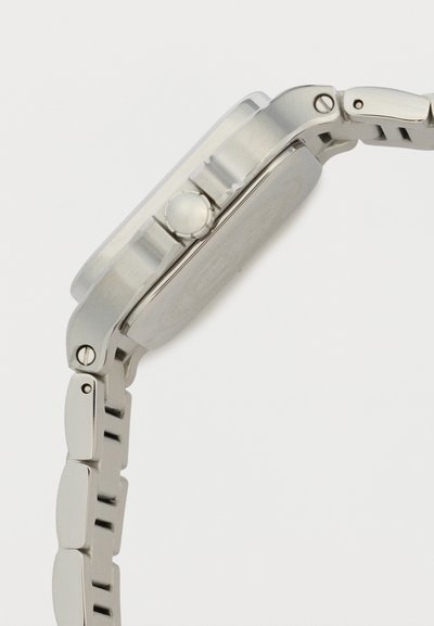 Vedere laterală a unui ceas de mână din metal argintiu, prezentând coroana, spatele carcasei și brățara legată, pe un fundal alb simplu.