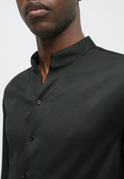 Musta napillinen paita, jossa on seisomakaulus, tekstuurinen kangas ja kuusi napin suljinta. Tyylikäs muotoilu minimalistisella estetiikalla.