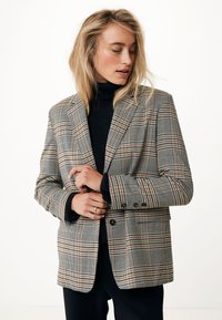 Blazer a quadri nei toni di marrone, nero e crema, con spalle strutturate, chiusura a doppio bottone e tasche laterali. Tessuto testurizzato.