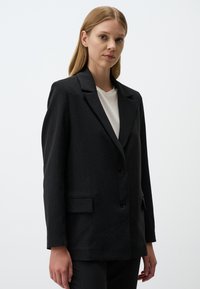 Blazer nero a righe sottili con rever a punta, chiusura a un bottone e tasche frontali. Il tessuto ha una consistenza liscia e una vestibilità sartoriale.