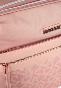 Bolso DKNY rosa claro con tejido suave y un patrón de monograma, un bolsillo con cremallera en la parte frontal y una placa de logo metálica.