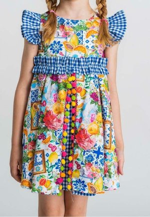 Robe fleurie colorée avec des volants en vichy bleu, des accents en pompons et un design à motifs mixtes, présentant des imprimés vifs de fruits et de fleurs.