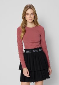 Langsleeve, rozenkleurig top gecombineerd met een zwarte, geplooide rok met een gegomde tailleband met de opdruk "BIZUU".