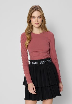 Langsleeve, rozenkleurig top gecombineerd met een zwarte, geplooide rok met een gegomde tailleband met de opdruk "BIZUU".