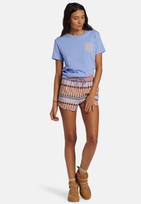 Camiseta de algodón azul claro con un estampado gráfico, combinada con pantalones cortos de patrón multicolor. El conjunto se complementa con botas de tobillo en color camel.