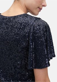 Granatowa bluzka wyszywana cekinami o teksturowanej, połyskującej powierzchni, z krótkimi, falbanistymi rękawami i okrągłym dekoltem, podkreślająca detale cekinowe.