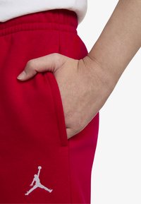 Sarkani sporta bikses ar redzamu roku kabatā. Raksturīga teksturēta auduma virsma un balts Jumpman logo uz augšstilba. Elastīgs jostasvīrs.