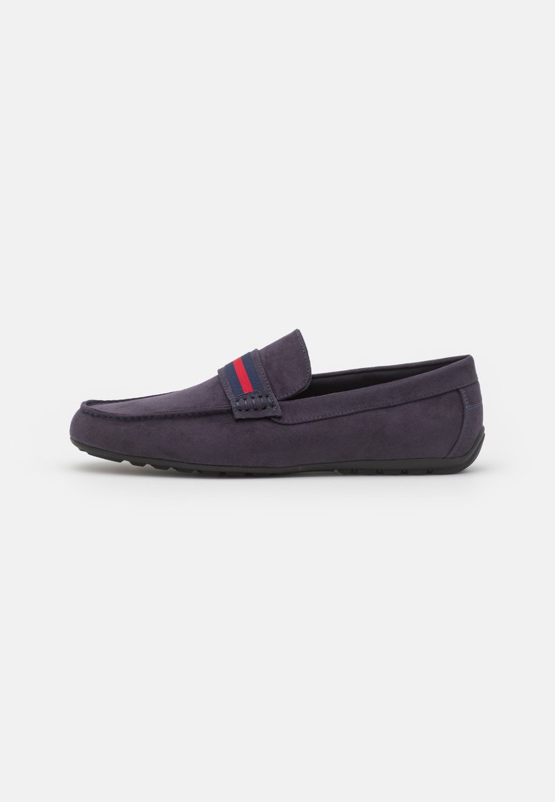 Mocassin en daim bleu marine avec semelle en caoutchouc et bride décorative à rayures rouges et bleues, vu de côté sur fond blanc.